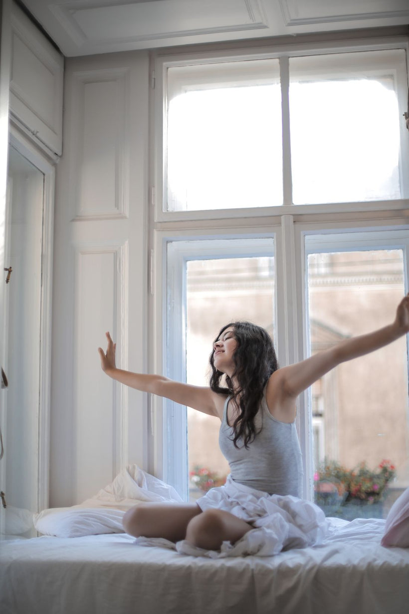 Woman stretching in bed, waking up refreshed in warm morning sunlight